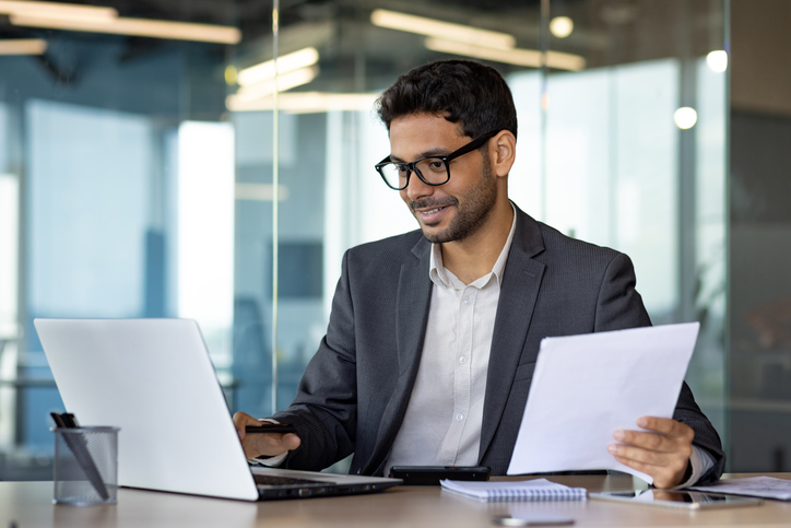 Cheerful male accountant in a suit doing paperwork in an office after completing his bookkeeper training