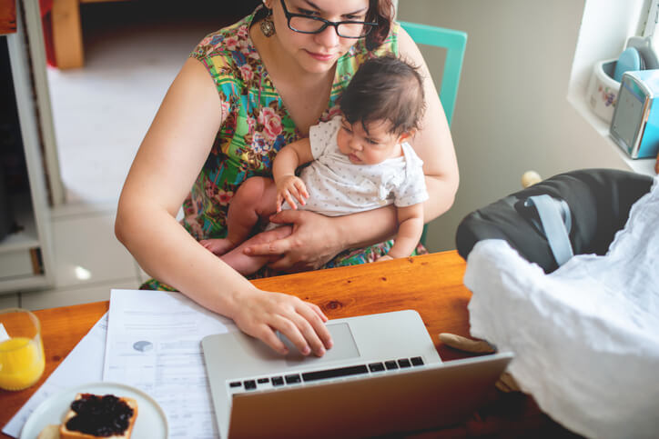 A career training program grad working on coursework at home while holding her baby