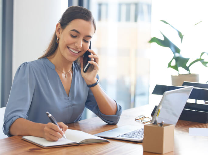 Female administrative assistant communicating over the phone with a client after completing her career training in BC